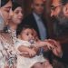 A touching moment during a baby's baptism ceremony, featuring a priest and family.