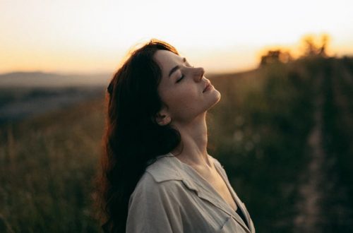A serene woman with head tilted back, savoring the warm sunset in a field.